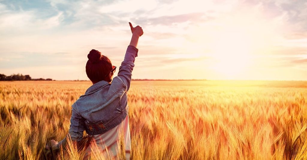 person in field at sunrise with thumbs up