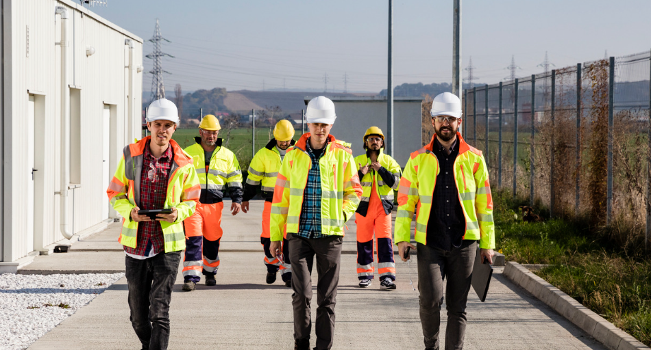 six field technicians in hi visibility gear and hard hats outdoors standing in a staggered formation