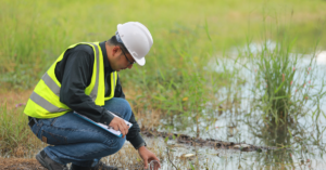field chemist in high visibility vest and hard hat tests water in wetland environment