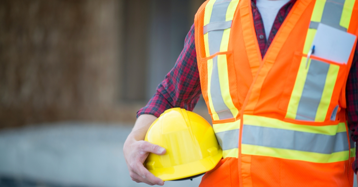 construction professional in hi viz vest holds yellow hard hat