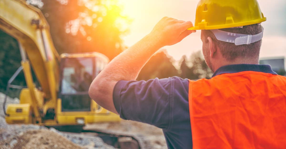 construction worker in hi viz vest and hard hat looking at earth digger equipment